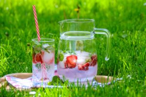 glass and pitcher of infused water with strawberries and mint on grass