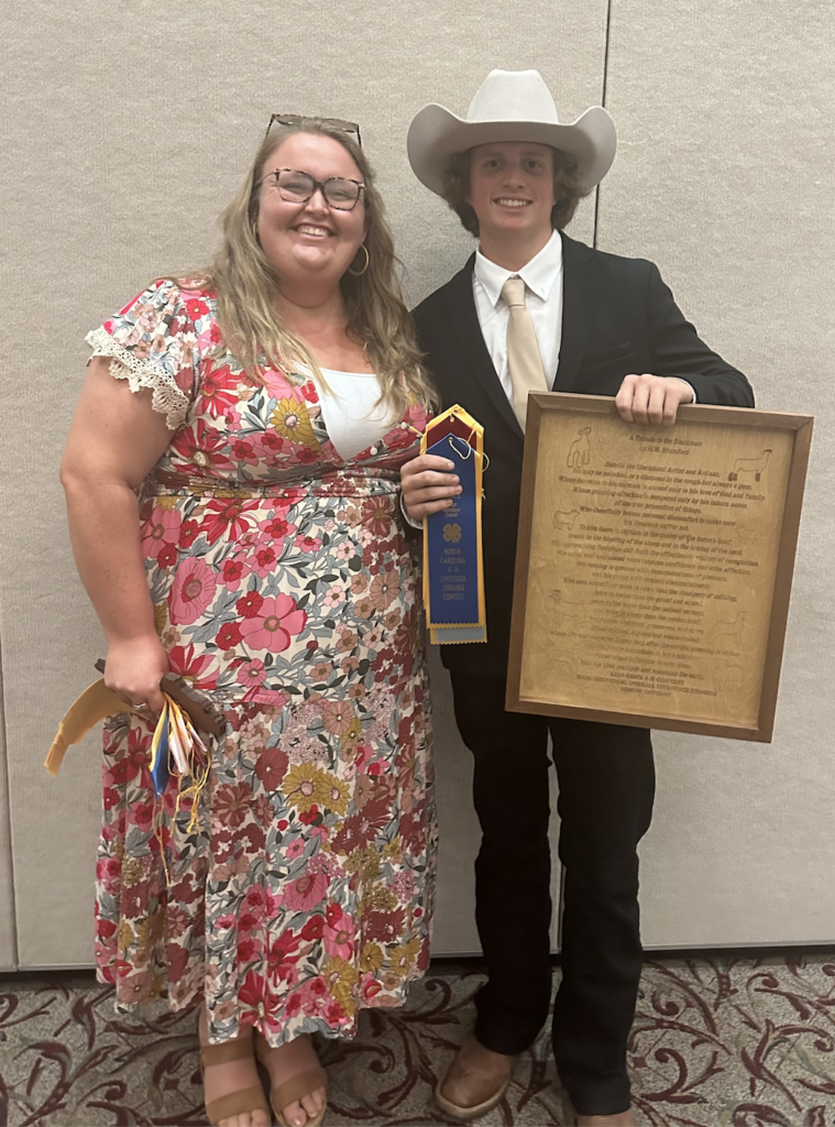 An adult and a teenager in a suit pose with awards.