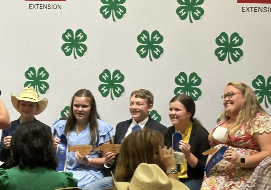 Kids pose with awards in front of a 4-H Banner.