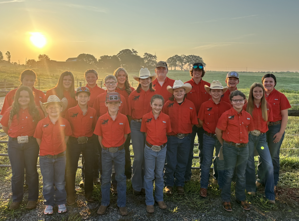 A group of kids in matching shirts pose together in a field.